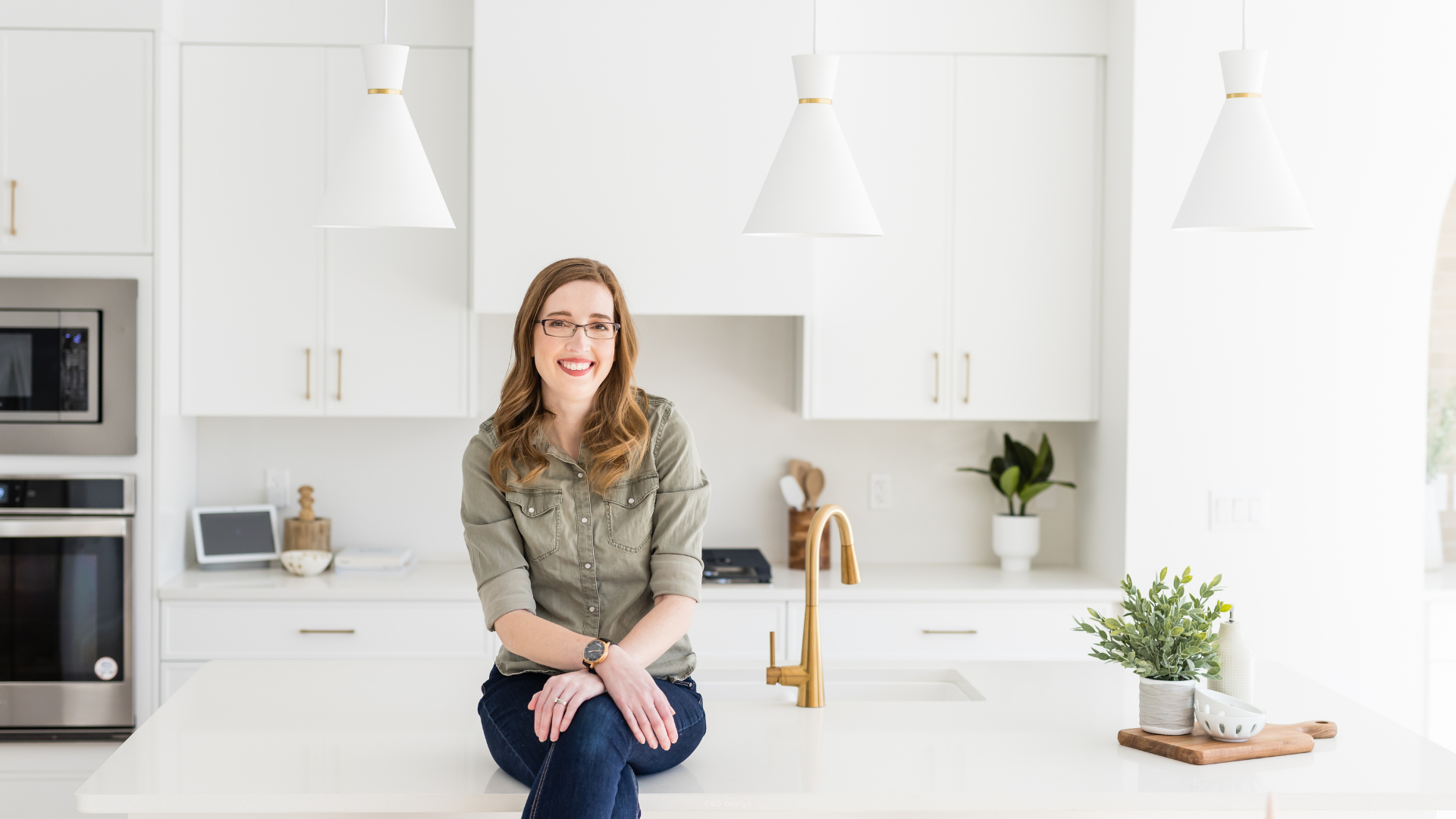 Chelsey from EBO Design sitting on a white quartz kitchen island countertop in a modern custom kitchen.
