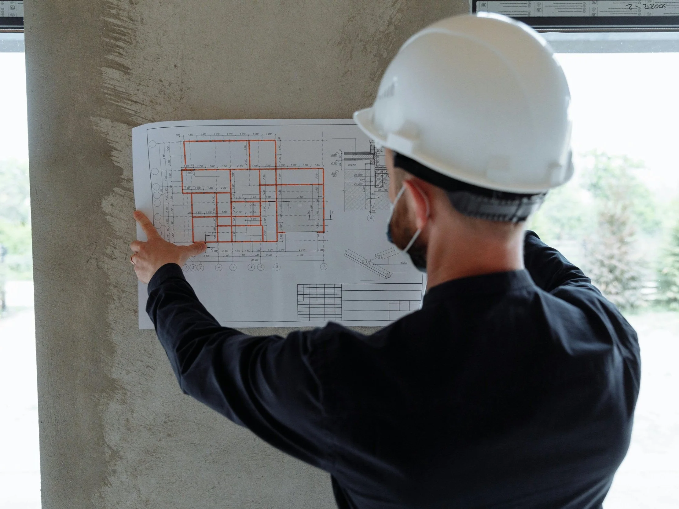 Contractor reviewing architectural floor plans on a job site during a home renovation project, wearing a hard hat and inspecting layout details.