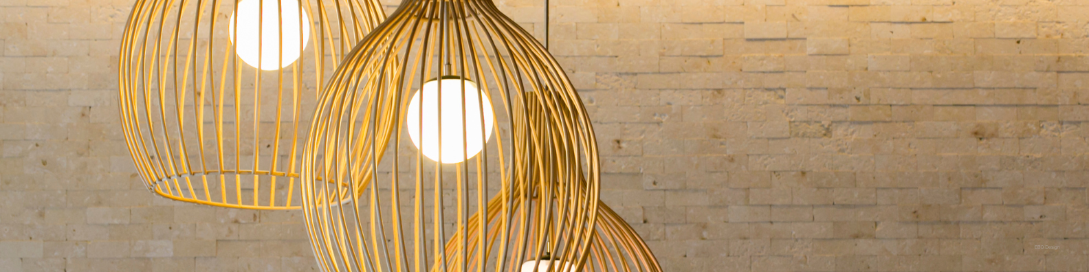 Modern gold pendant lighting with round bulbs hanging against a natural stone wall. The warm glow and sculptural design create an elegant, contemporary interior focal point perfect for modern home lighting inspiration.