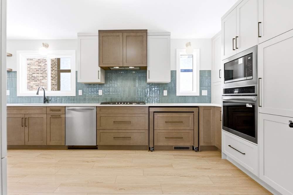 Kitchen elevation view showing a mix of grey and wood cabinets, built-in stainless steel microwave and wall oven, and a wood rolling island cart stored neatly under the counter.