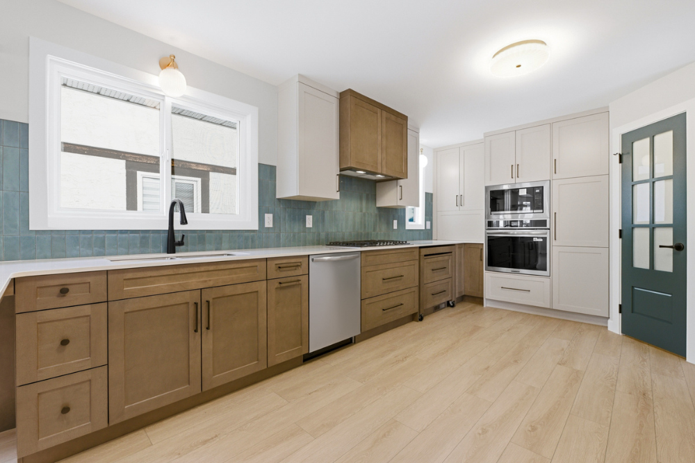 A wide-angle, low perspective shot looking down the main counter run of a kitchen, showcasing the dark wood base cabinets, the white countertops, the modern black faucet, a stainless steel dishwasher, and a full-height teal square-tile backsplash. 
