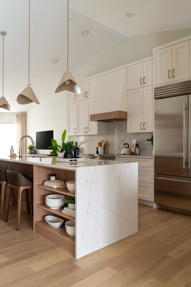 An angle shot highlighting the open wood shelving and marble waterfall edge of a large kitchen island, adjacent to leather barstools.