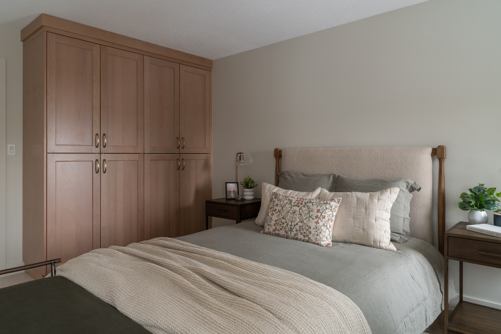 A corner shot of a bedroom featuring a large, four-door wooden armoire (wardrobe) next to a bed with neutral bedding and a nightstand.