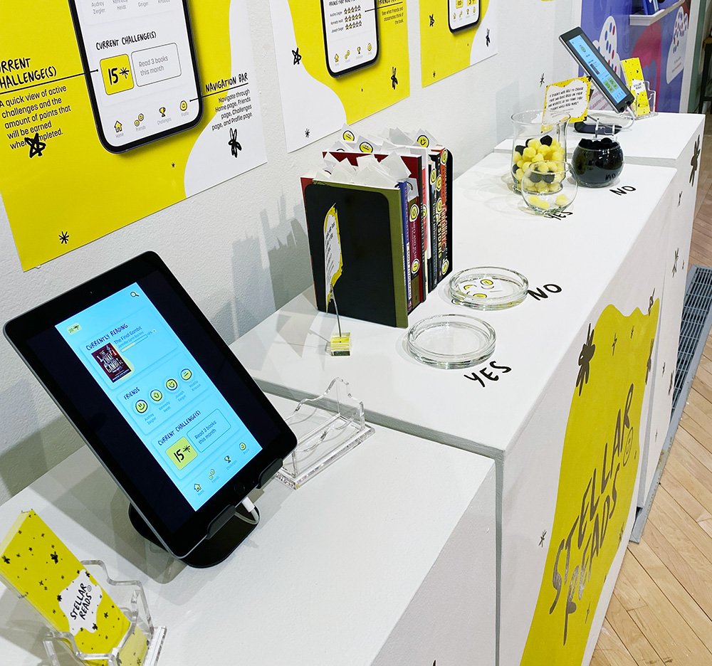 Stellar Reads display with tablets showing the app, posters on the wall, books, and interactive jars labeled Yes and No.