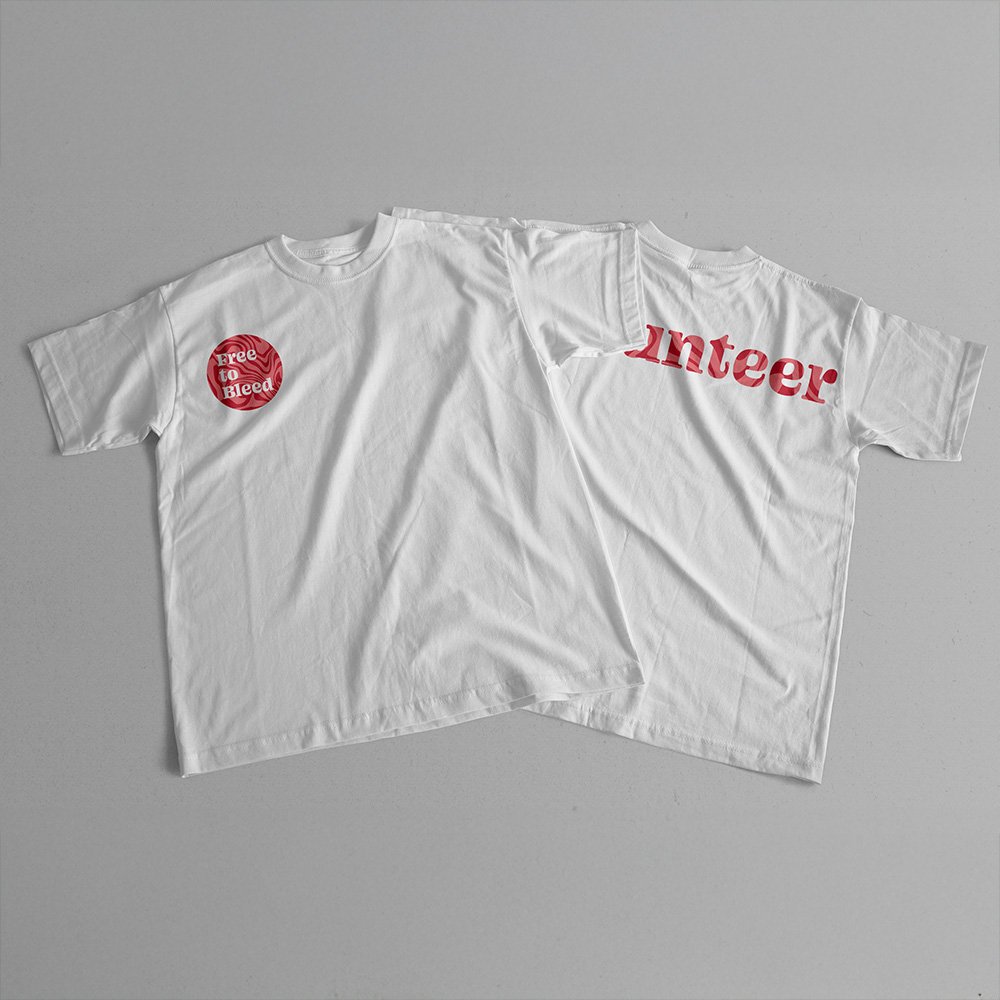 Two white T-shirts displayed flat, one with a red “Free to Bleed” circular logo on the chest and the other showing partial red lettering on the back, that reads "Volunteer"