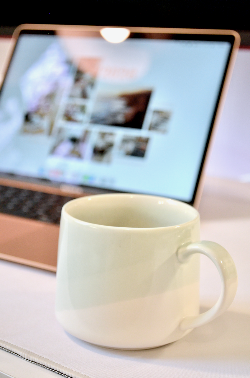 A small mint green coffee cup sits in focus with a Macbook behind it, slightly blurred.