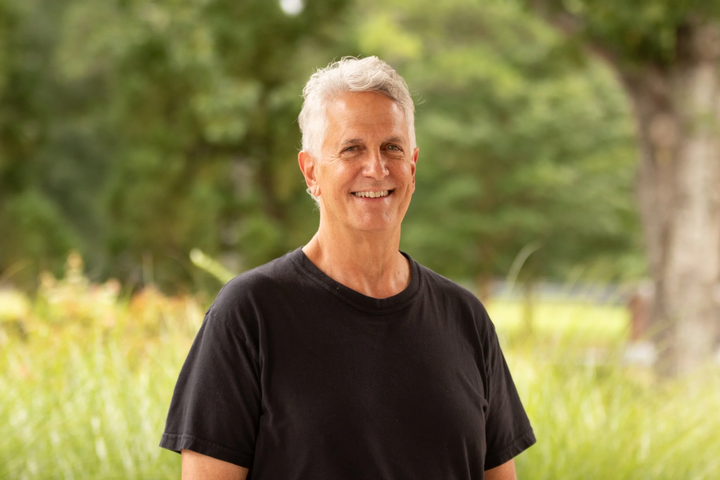 Smiling middle-aged man with gray hair wearing a black shirt against a plain background.