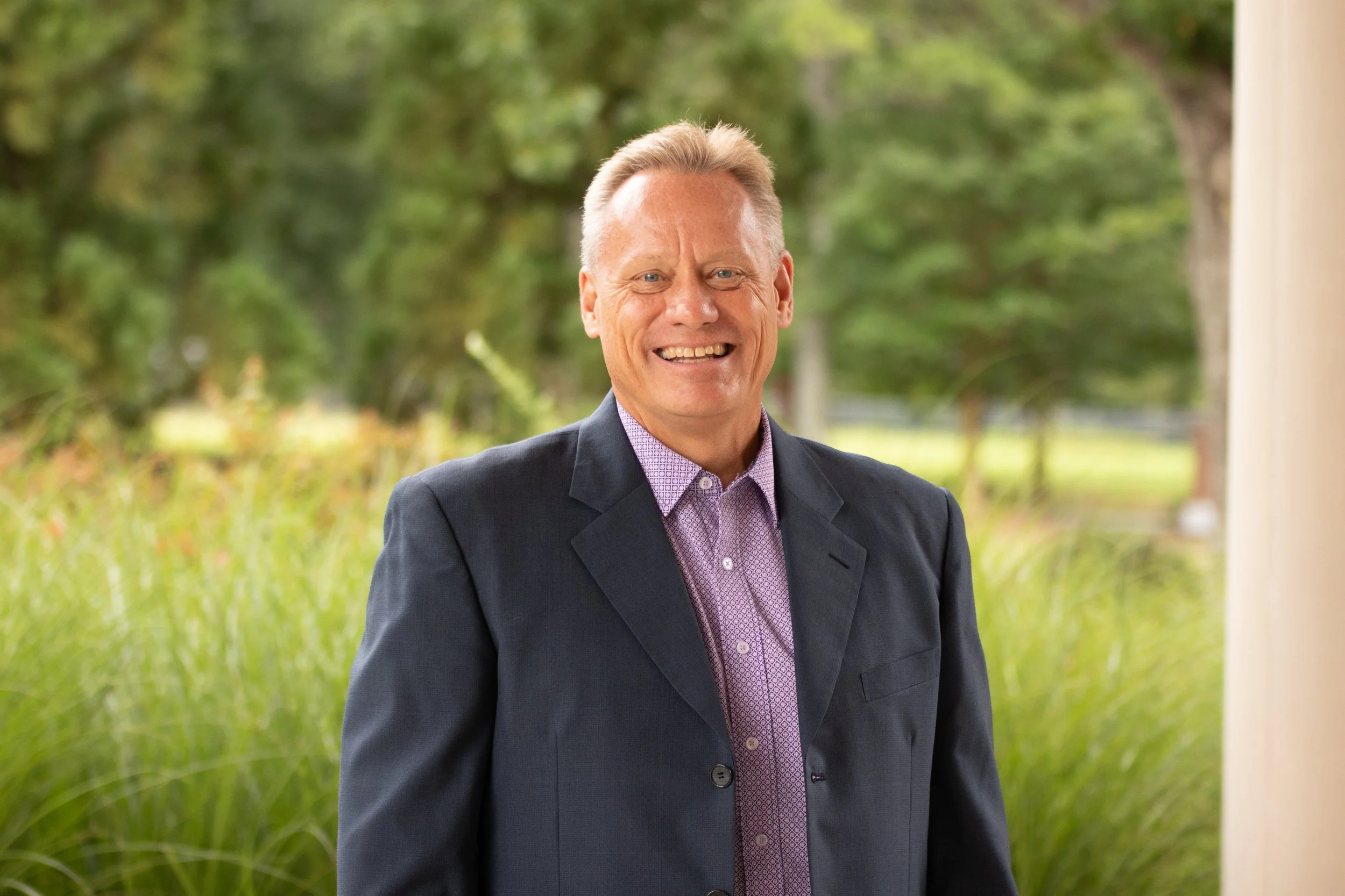 Close-up of a middle-aged man with a short haircut, smiling outdoors in front of a church.