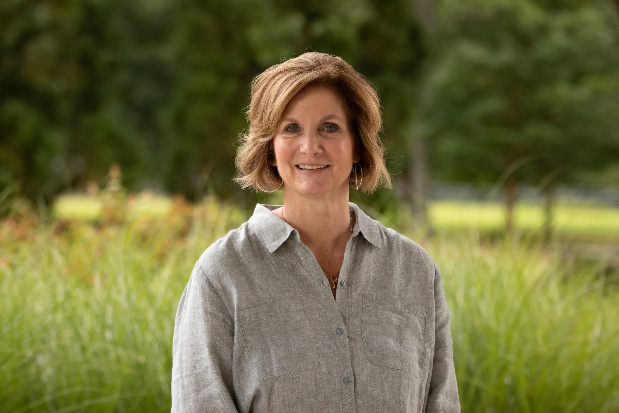 Portrait of a smiling woman with short brown hair, wearing a brown jacket, against a neutral background.
