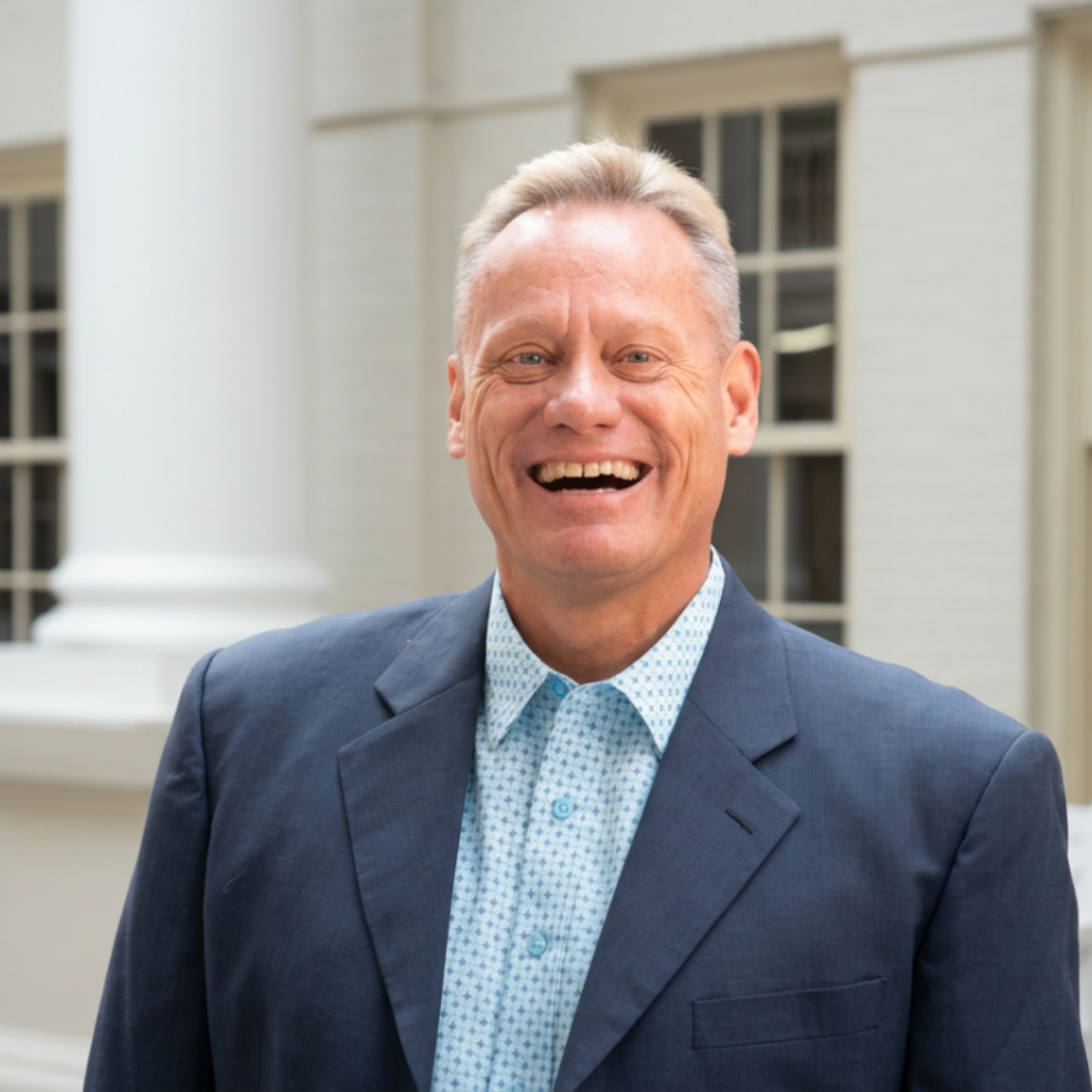 Close-up of a middle-aged man with a short haircut, smiling outdoors in front of a church.