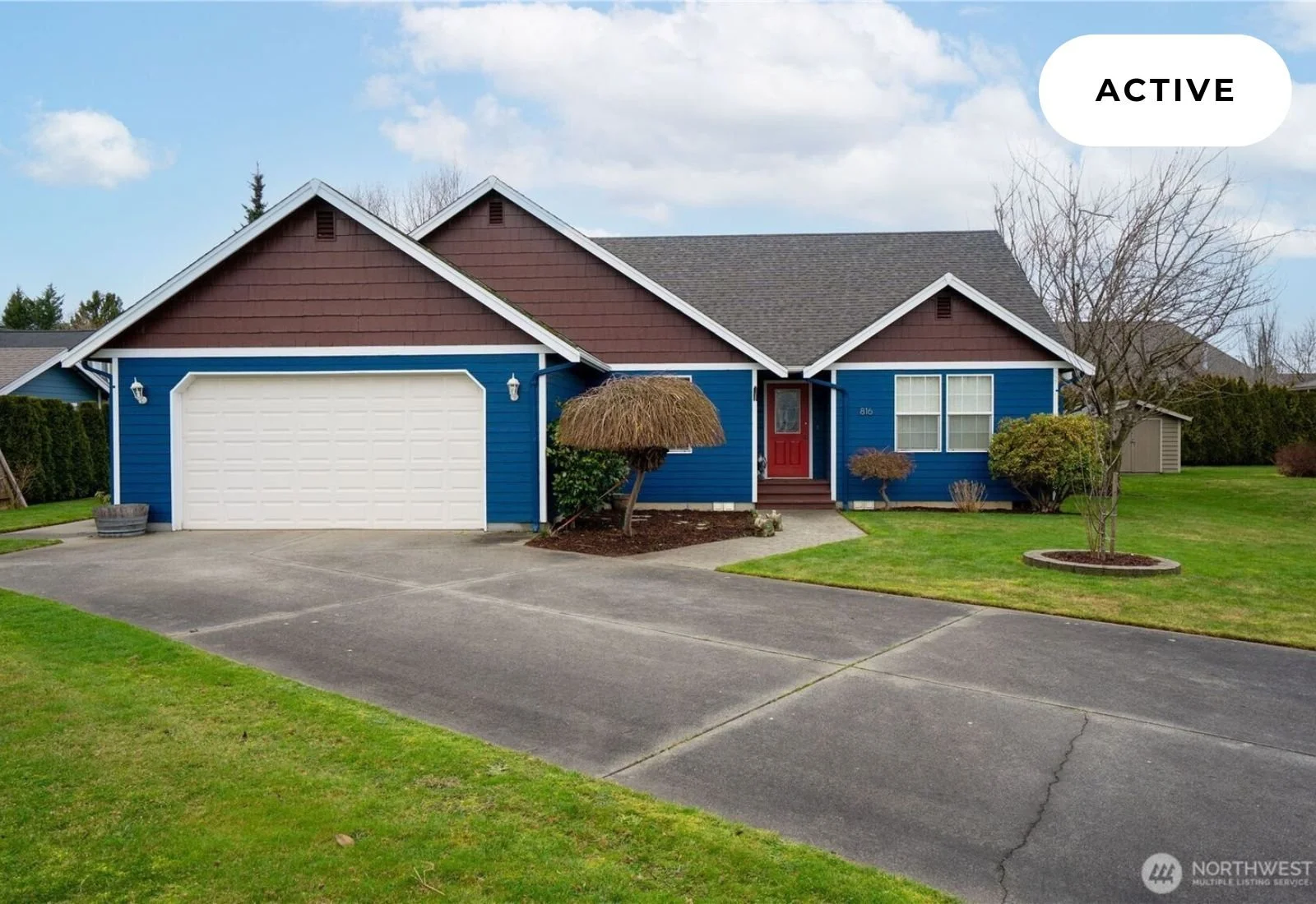 Colorful house with blue siding, brown accents, red front door, attached garage, front lawn, leafless trees, driveway, and cloudy sky, labeled as active.