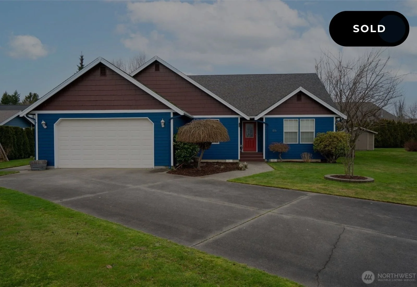 Colorful house with blue siding, brown accents, red front door, attached garage, front lawn, leafless trees, driveway, and cloudy sky, labeled as active.