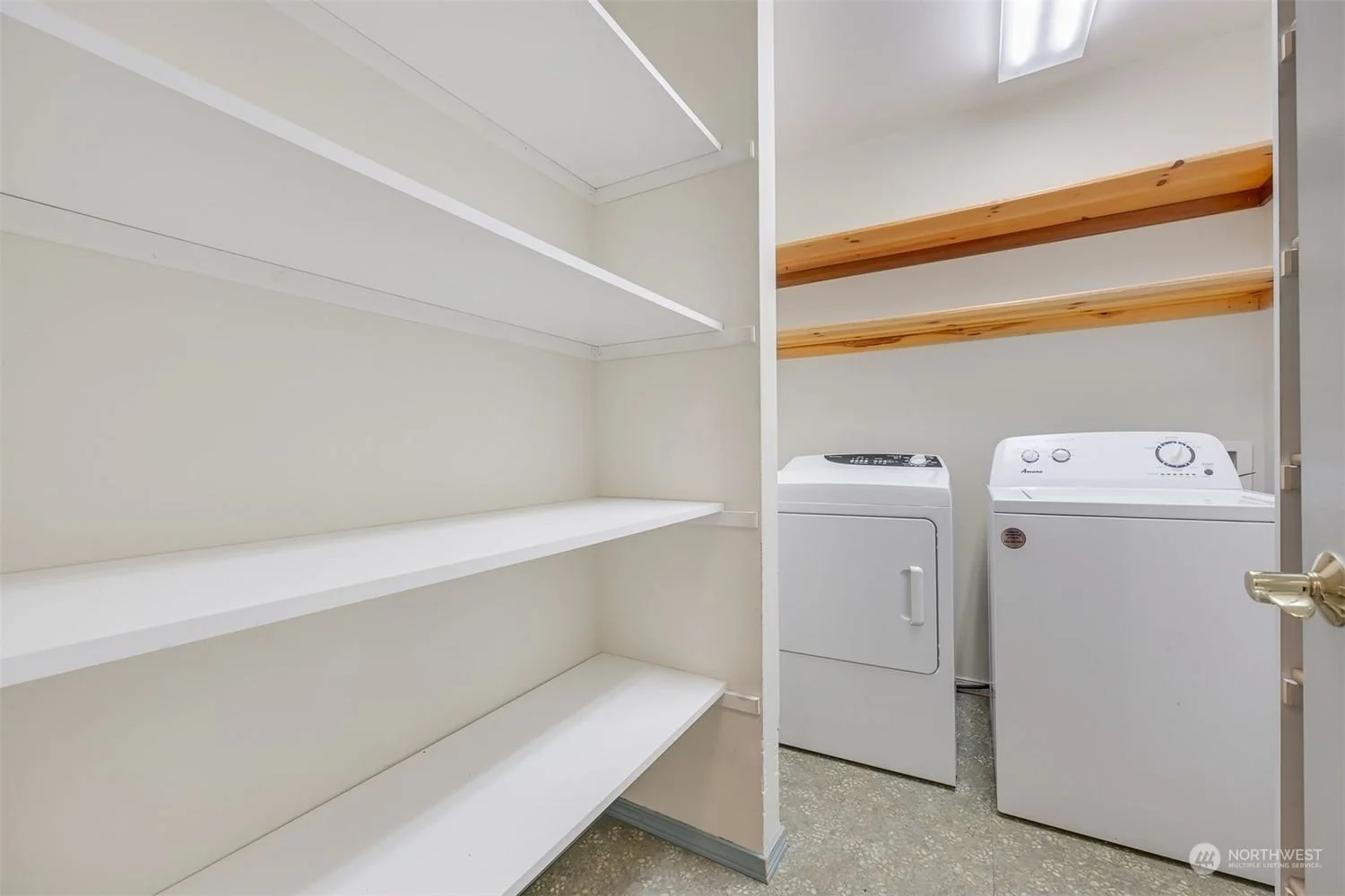 Laundry room with empty white shelves and a washer and dryer with wooden shelves above.