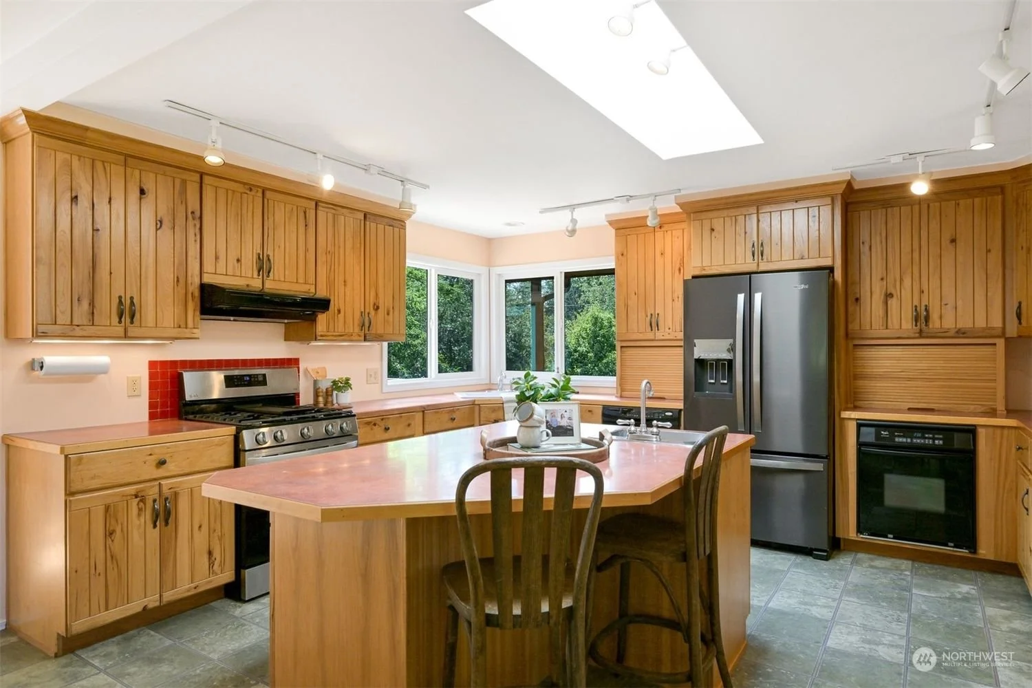 Wooden kitchen with island, stainless steel appliances, and large window overlooking greenery.