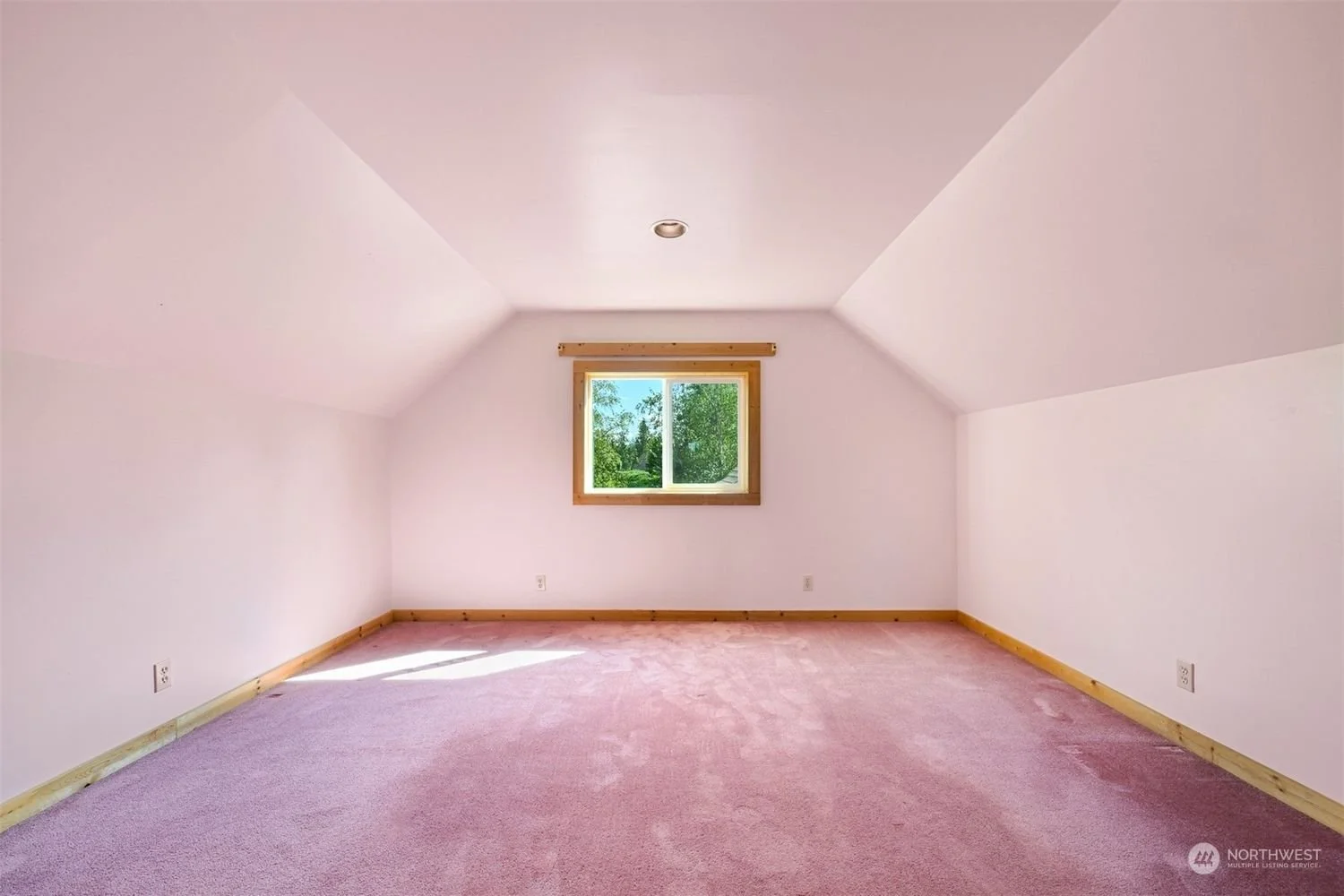 Empty bedroom with pink carpet, white walls, small window, and natural light, located in an attic space.