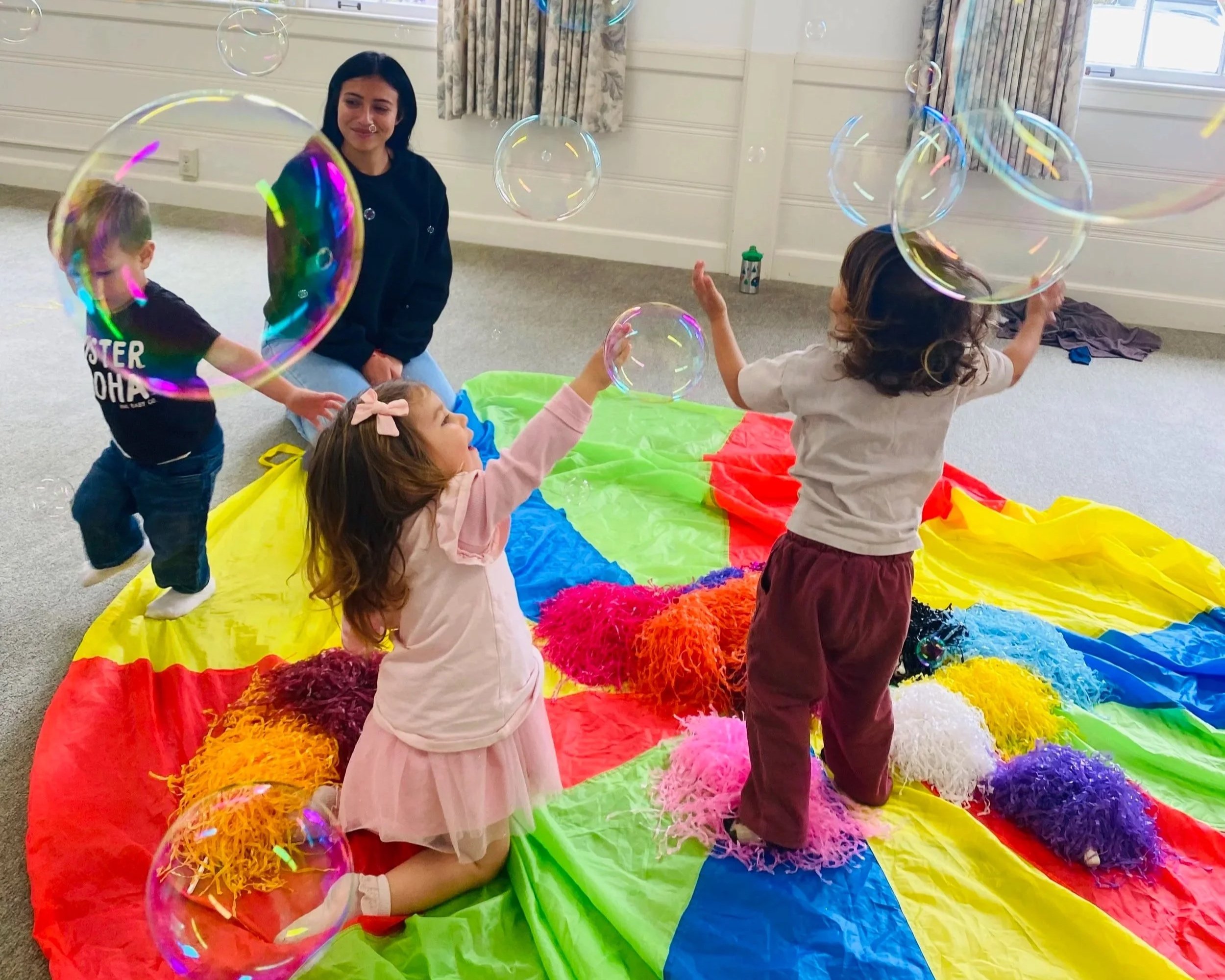 Toddlers playing in bubbles and a big parachute at Toddler Tumble Tunes in Carpinteria