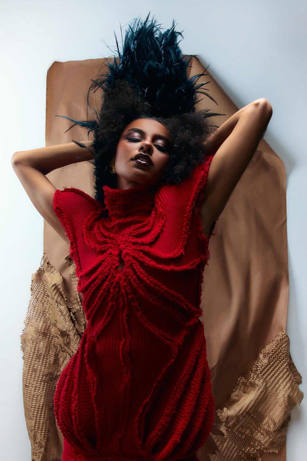 Fashion model poses for photography highlighting her red woven dress and dramatic black feather headpiece. 