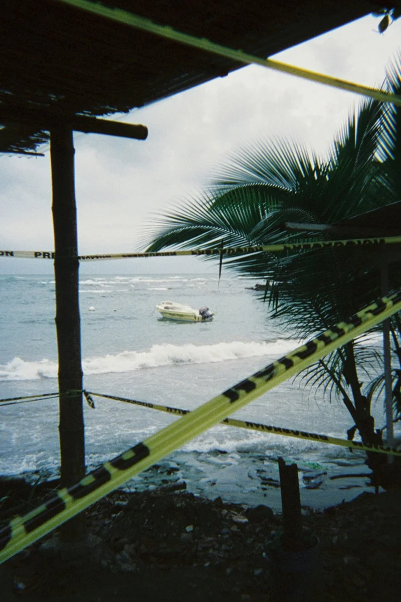 Beach scene with a small boat in the water, partially obscured by police tape and a palm tree.