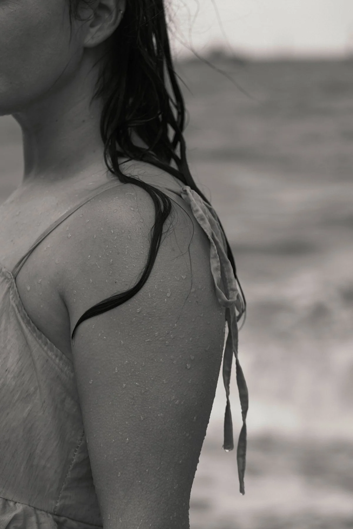 Close-up of a woman's shoulder and part of her face with wet hair, wearing a tank top at the beach, in black and white.