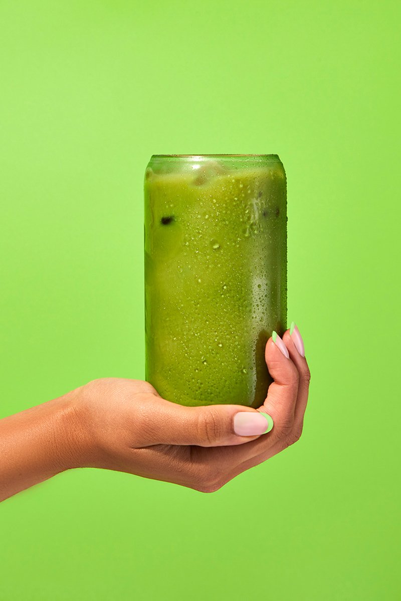 A hand holding a tall can of green beverage against a green background.