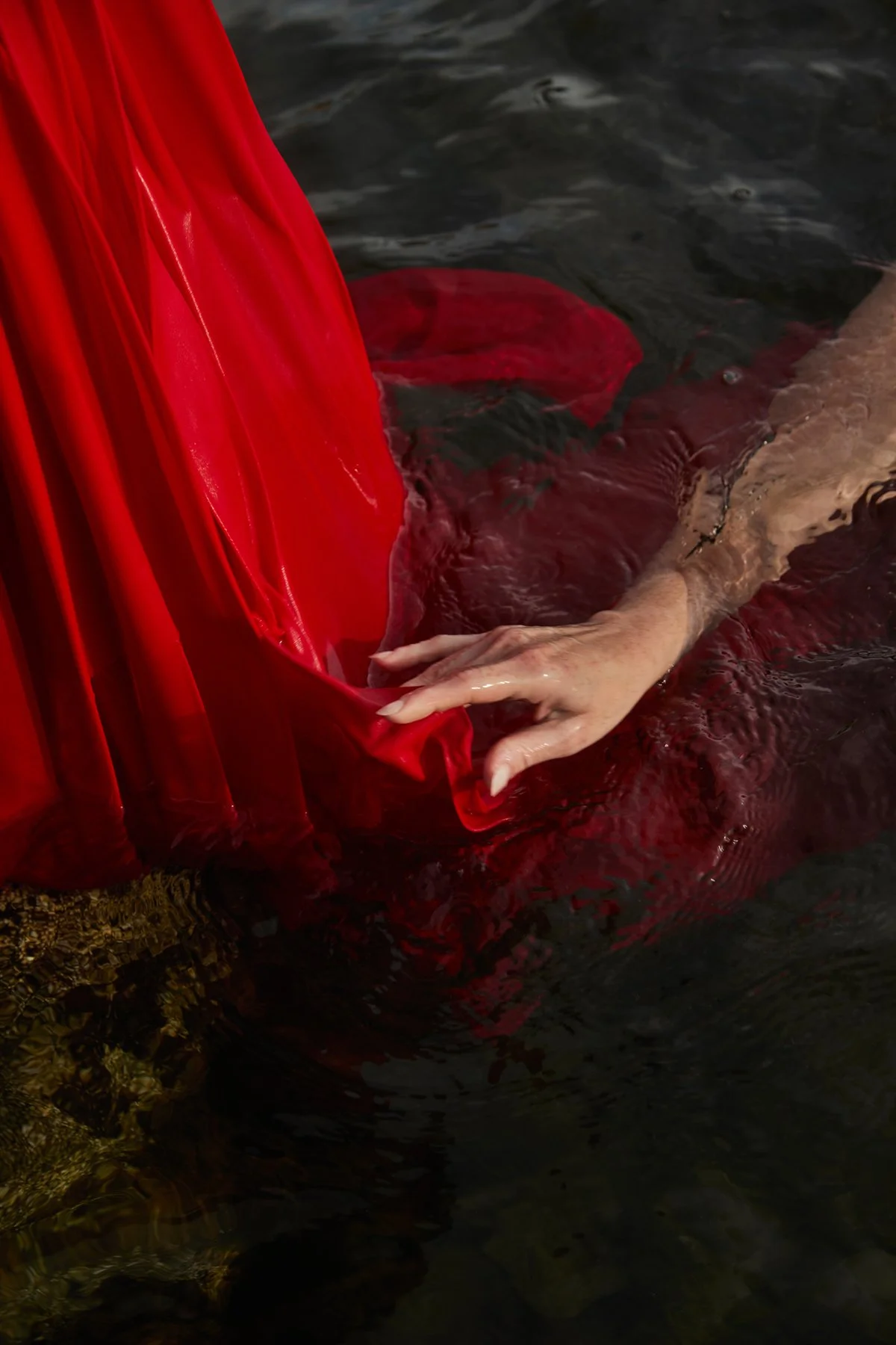 A person holding onto red fabric in water, with only their hand and arm submerged.