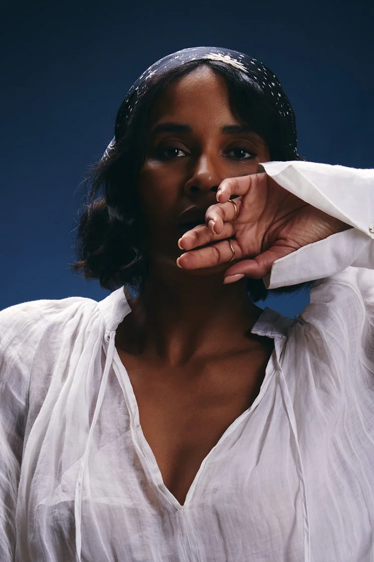 Fashion photograph of a woman in a white shirt holding her hand to her face. 