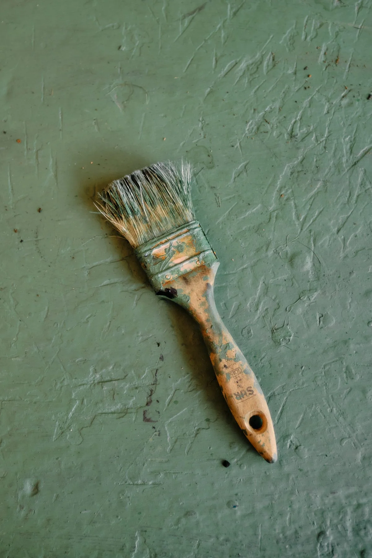 A weathered paintbrush with a worn handle lying on a green textured surface.