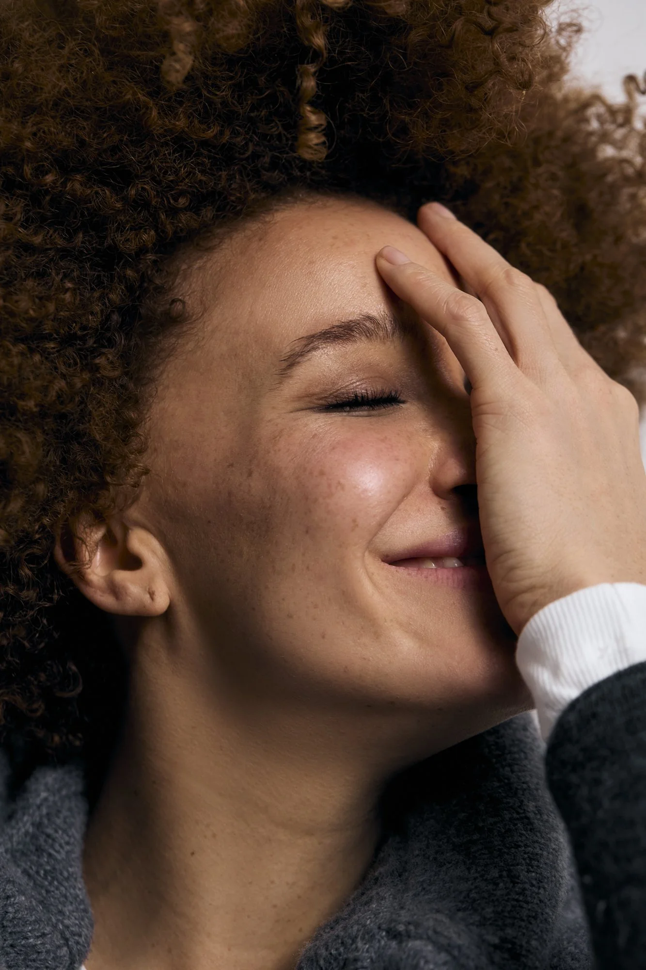 Beauty photography of a woman with curly hair smiling with her eyes closed.