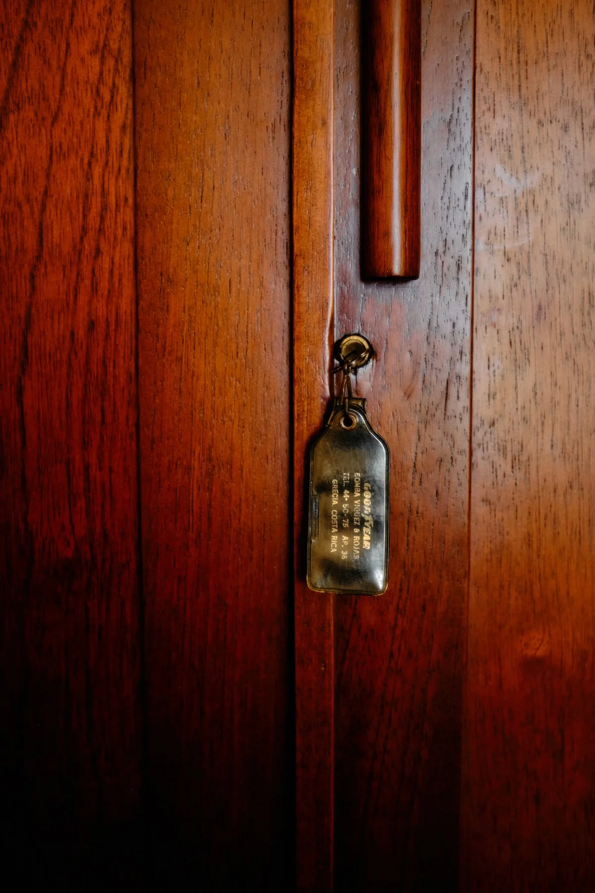 Close-up of a wooden cabinet door with a brass key and a vintage metal key tag hanging from the lock.