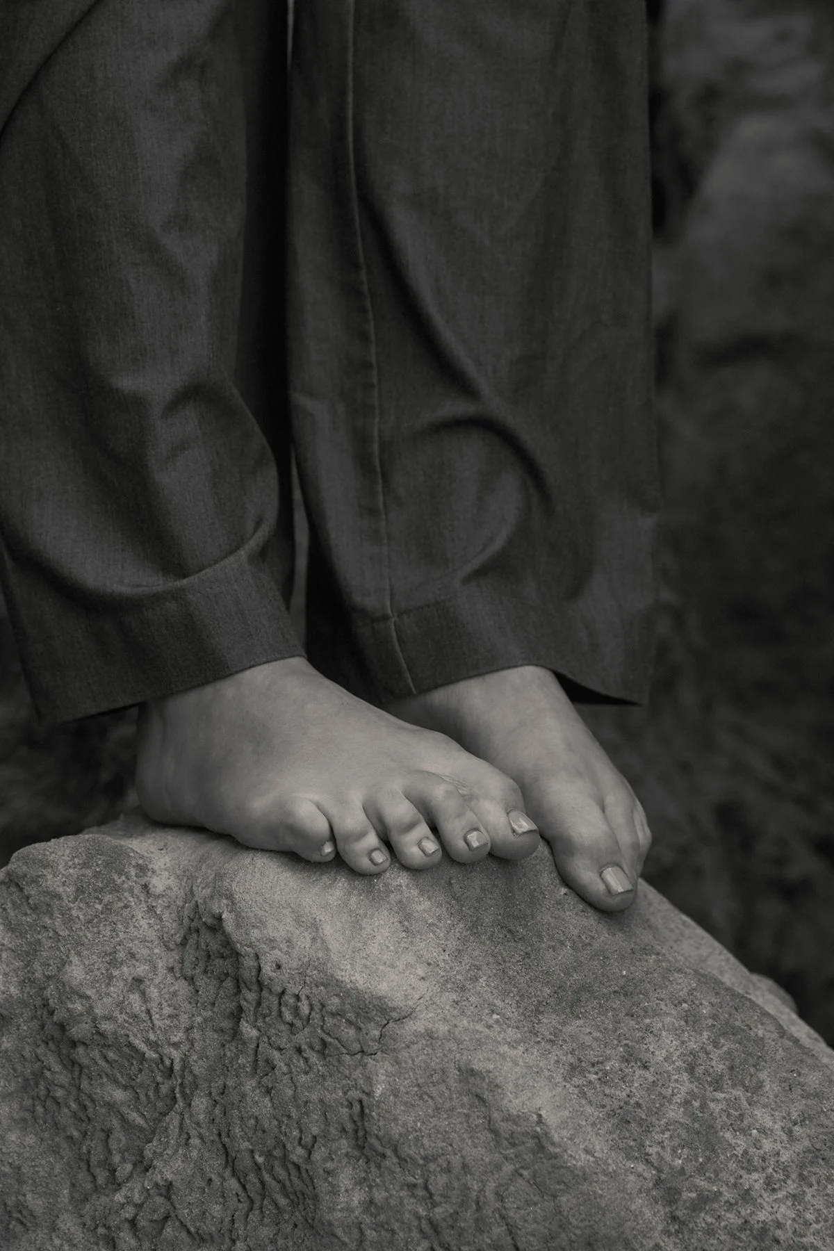 Close-up of a person's feet standing on a rock, wearing dark pants.
