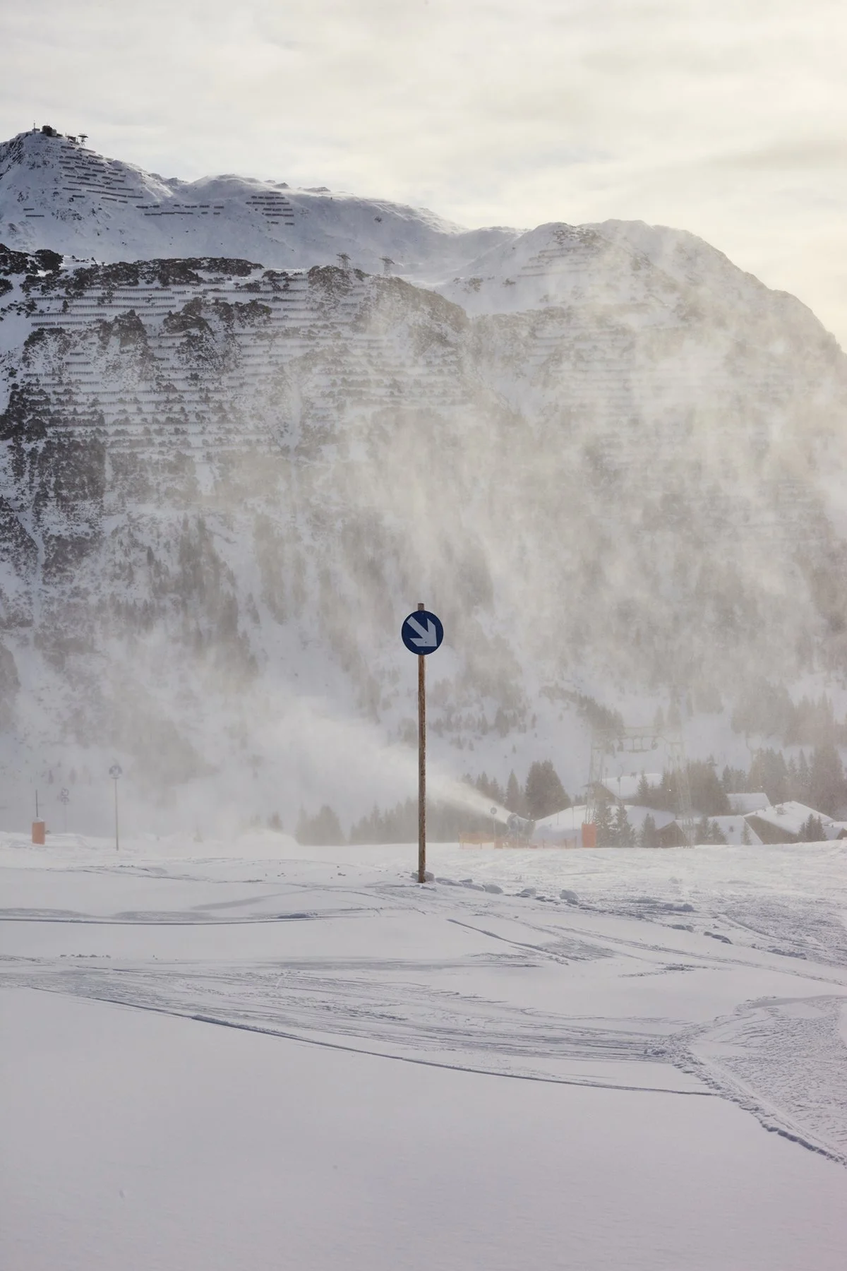 Snow-covered landscape with mountains in the background and a traffic sign in the foreground.