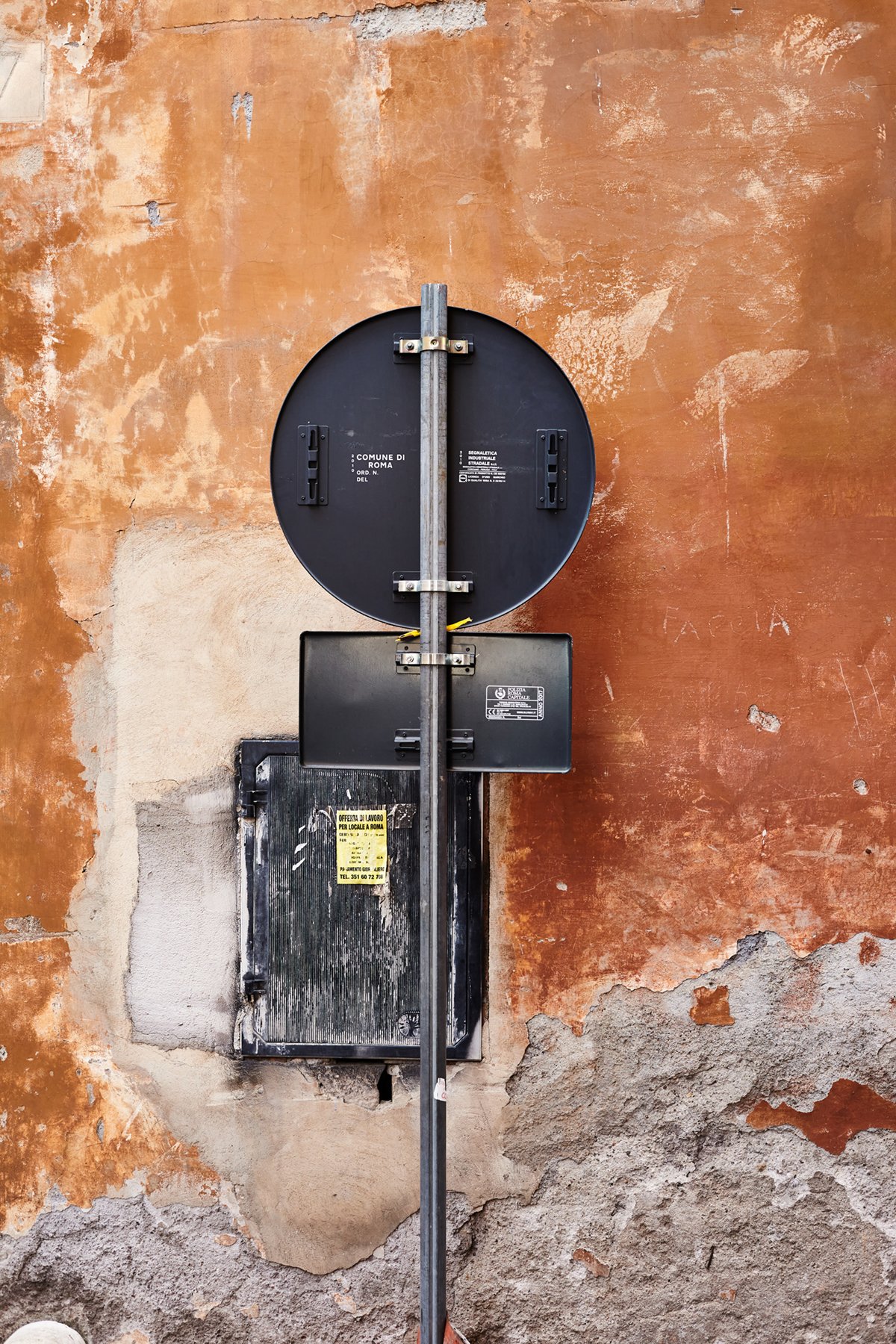 View of an unused traffic sign and electrical box mounted on a weathered, orange wall.