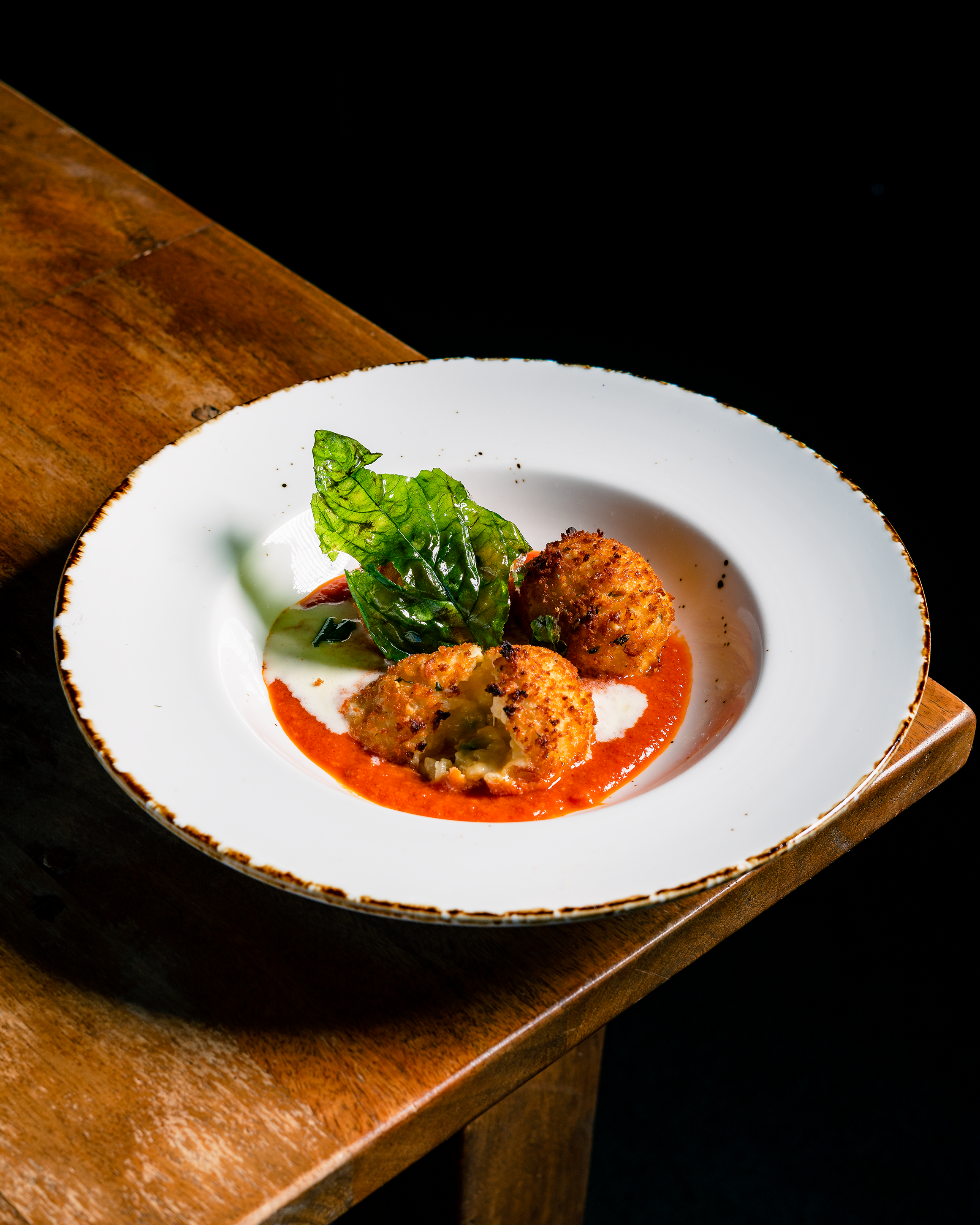 Three arancini balls on a white plate with red sauce and basil leaves, on a wooden table.