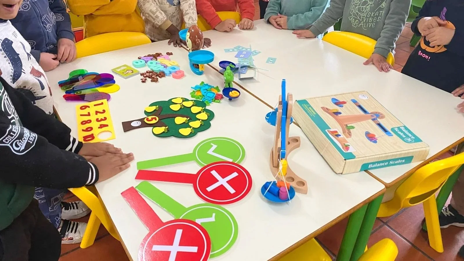 Grupo de crianças brincando com jogos e brinquedos educativos em uma mesa de recreação escolar.