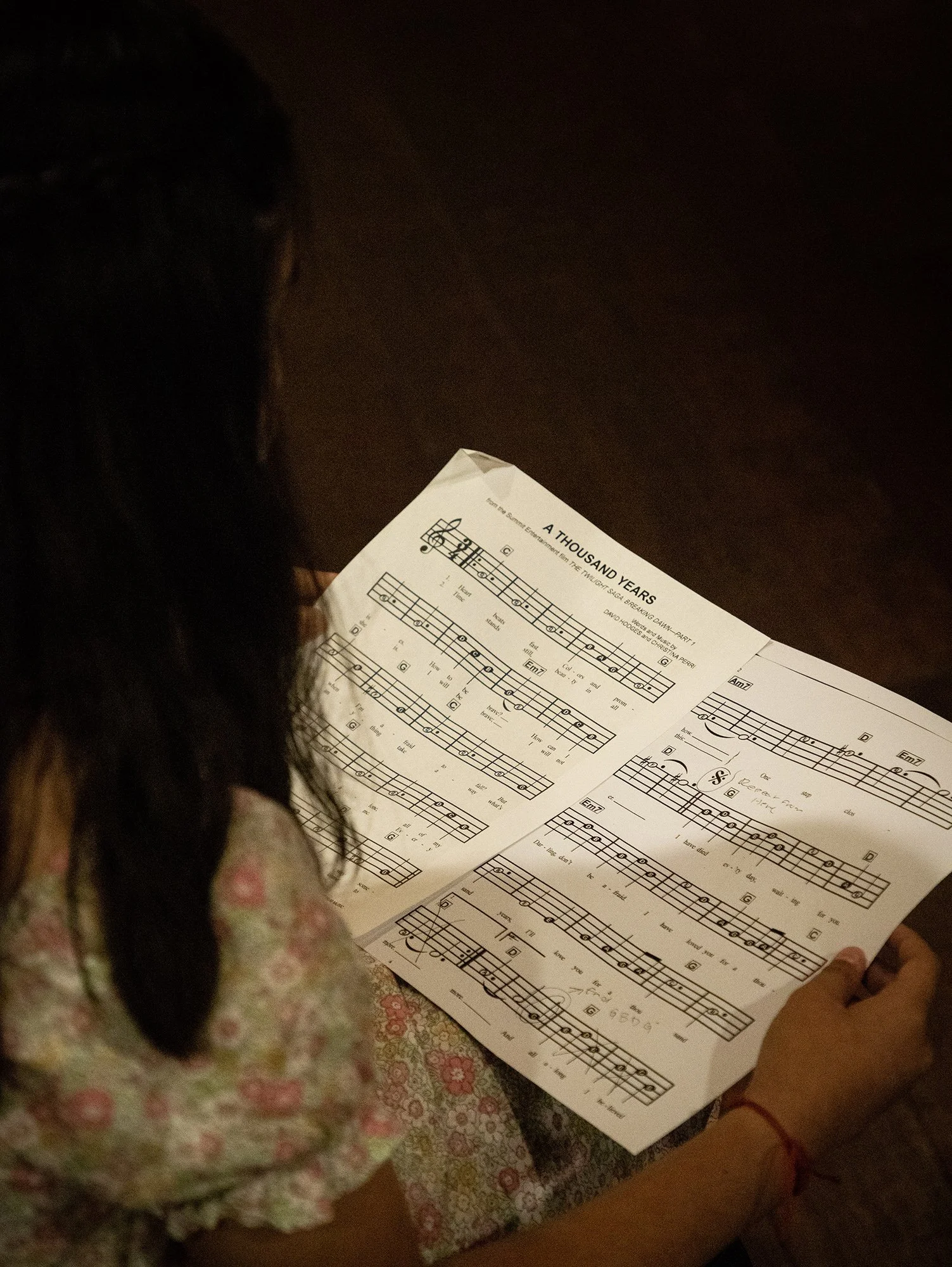A person with long dark hair reading sheet music titled "A Thousand Years".