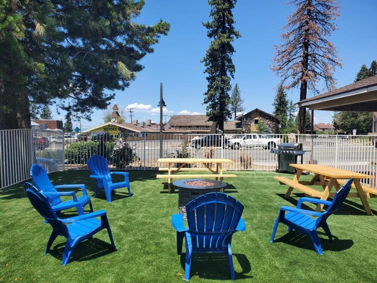 Outdoor patio area with lounge chairs arranged around a fire pit on a grassy lawn, fenced with a view of south lake tahoe. At Bluebird Day Inn & Suites