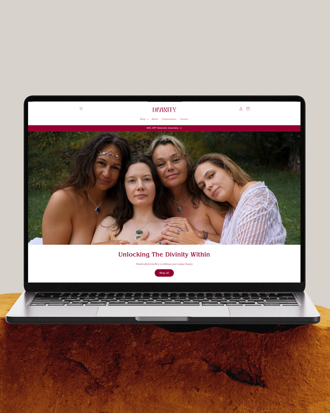 Laptop displaying a jewelry website 'Divinity' featuring four women in a natural setting, promoting handcrafted jewelry with the text 'Unlocking The Divinity Within.'