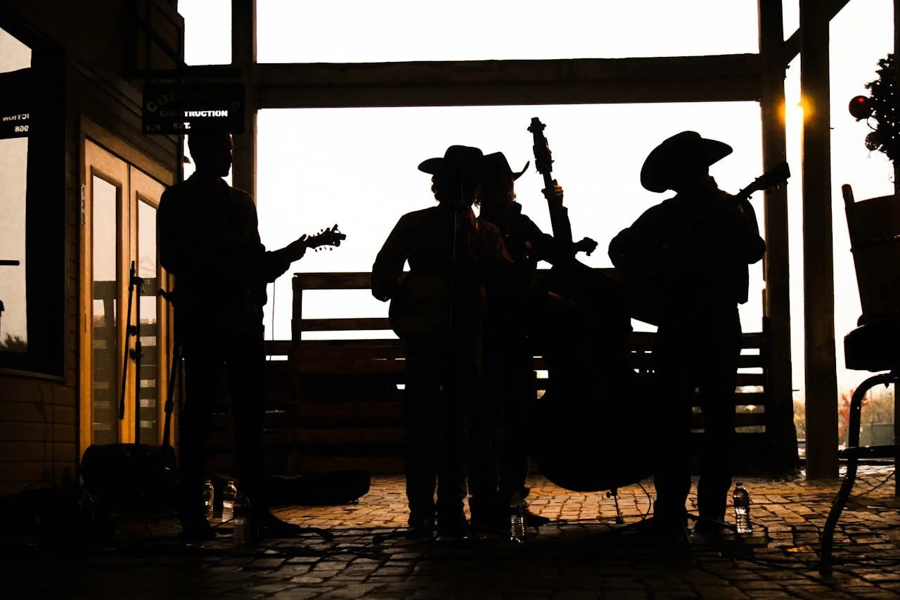 Four country musicians performing in a barn at dusk, their appearances masked by the shadows