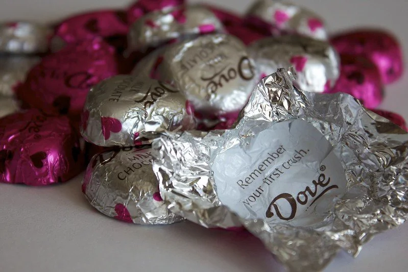 Several pieces of Dove chocolates, one piece is open revealing a wrapper that says "Remember your first crush"