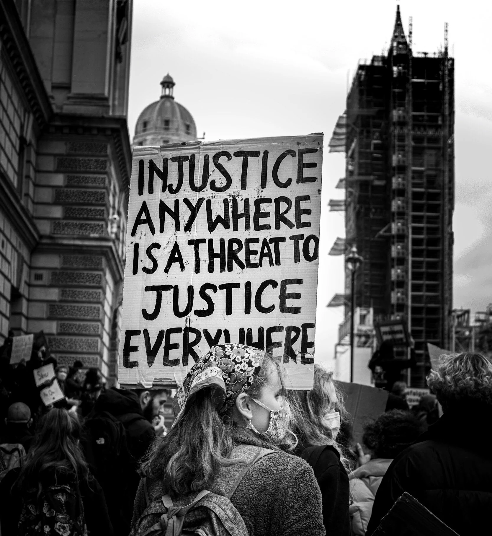 A black and white photograph of a protest march. A placard reads, "Injustice anywhere is a threat to justice everywhere."