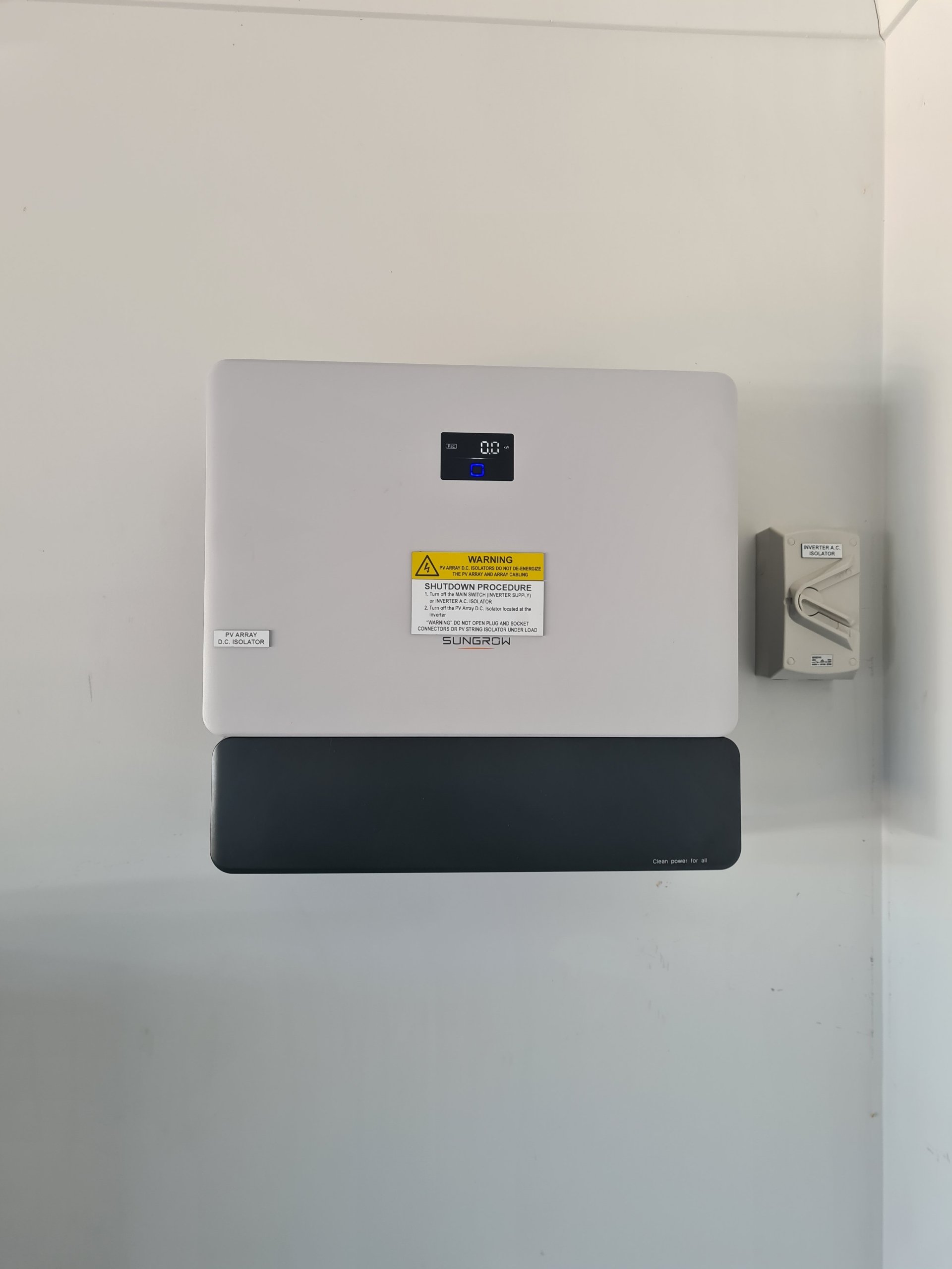 Wall-mounted solar inverter with a display, labeled "Sungrow," and a yellow warning sticker.