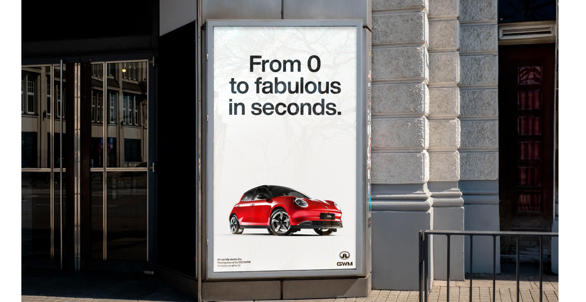 An outdoor ad for a red electric GWM Ora car with the text 'From O to fabulous in seconds.' The ad is located on the corner of a building, beside a sidewalk. The ad features a small, sporty, red electric car with black accents and a black roof.