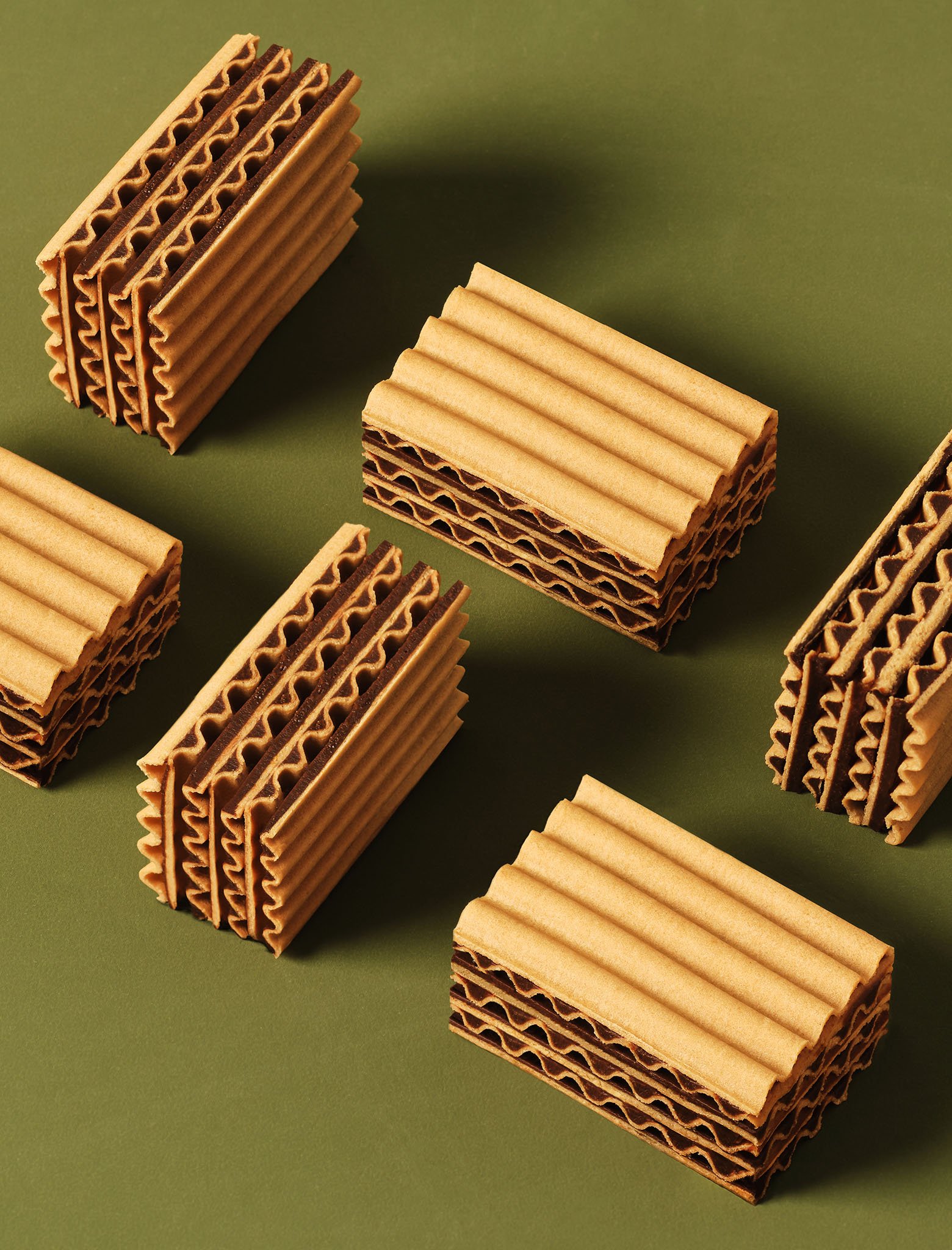 Multiple rectangular wafer cookies, with some containing chocolate filling, arranged on a green surface.