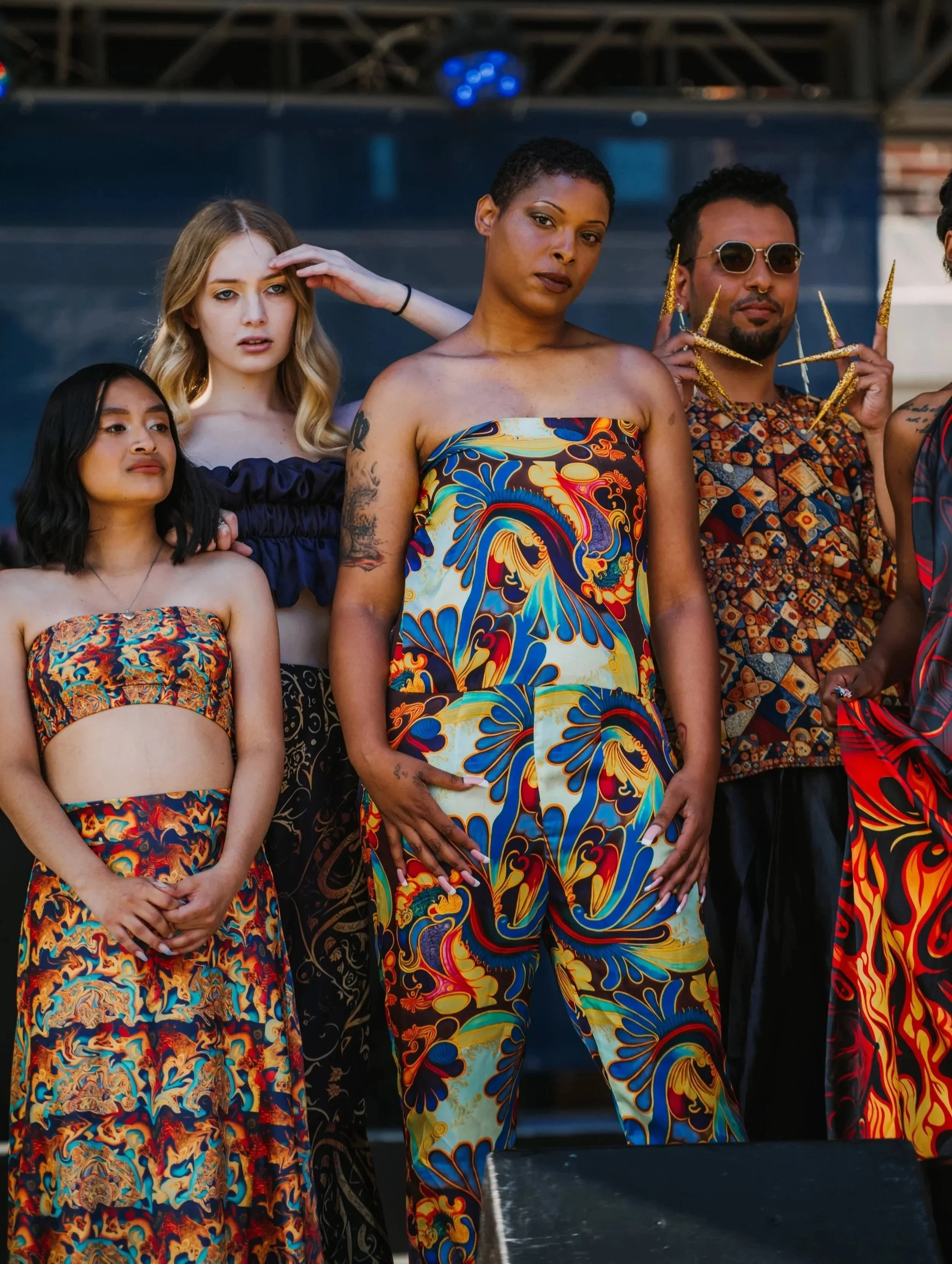Group of five diverse people standing on stage, wearing colorful patterned clothing, with some striking confident poses.