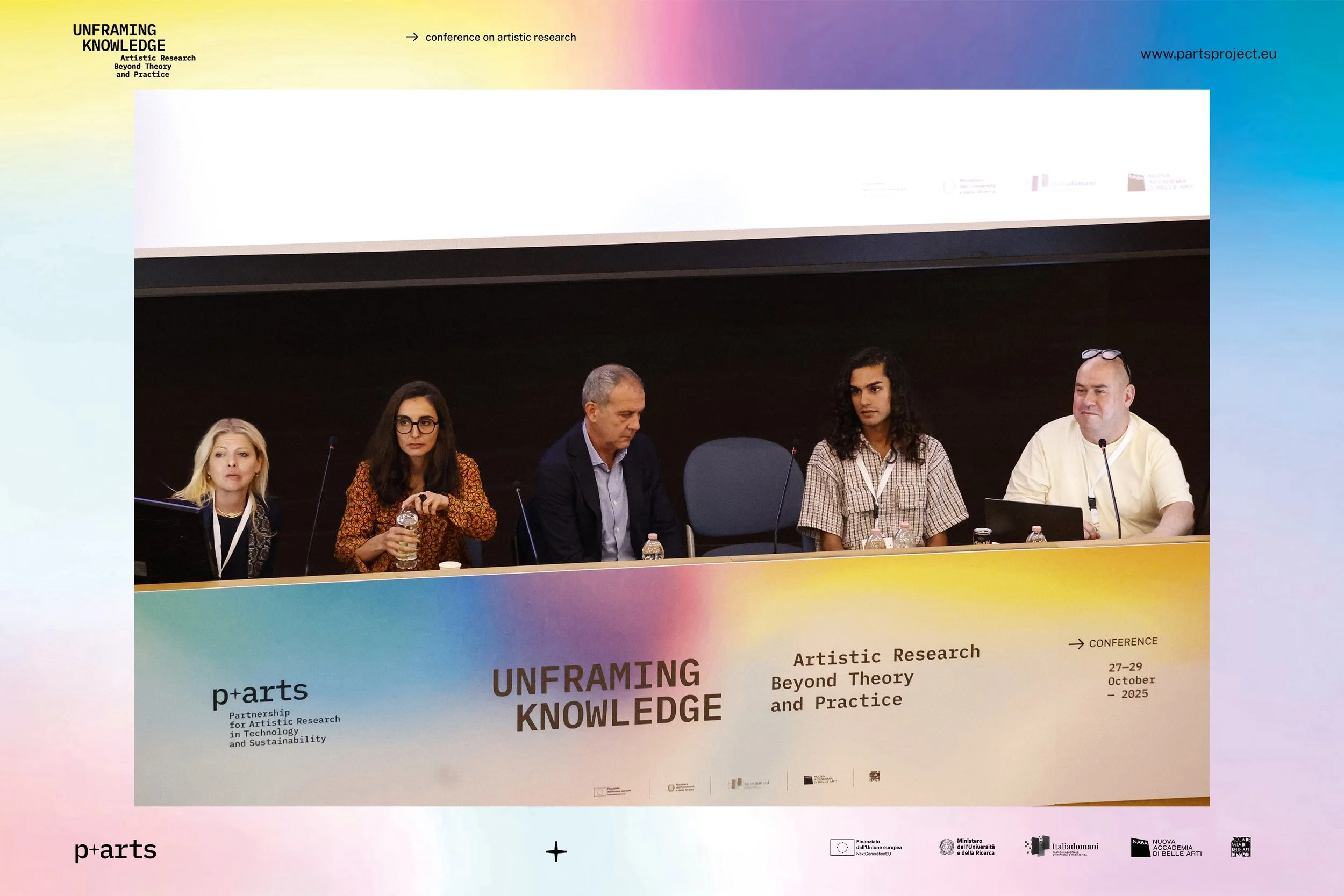 Five people seated at a long table during a conference on artistic research, with a large screen or wall behind them displaying conference information and logos.