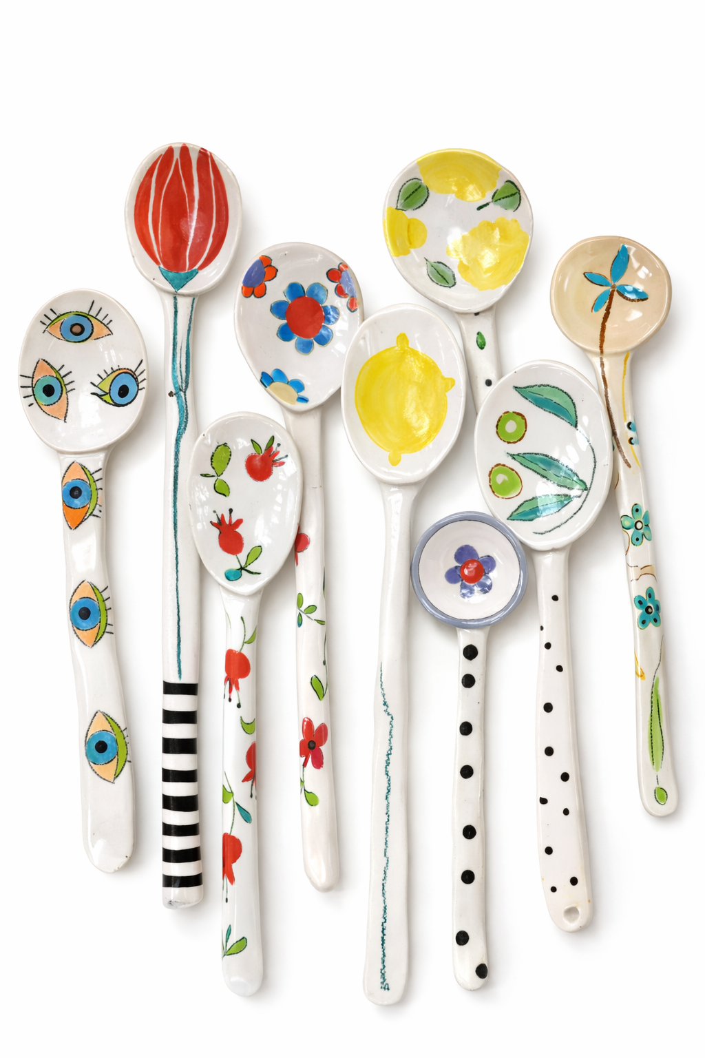 Cuillères en porcelaine décorées avec des motifs colorés, y compris des fleurs, des yeux, des fruits et des feuilles, sur un fond blanc.