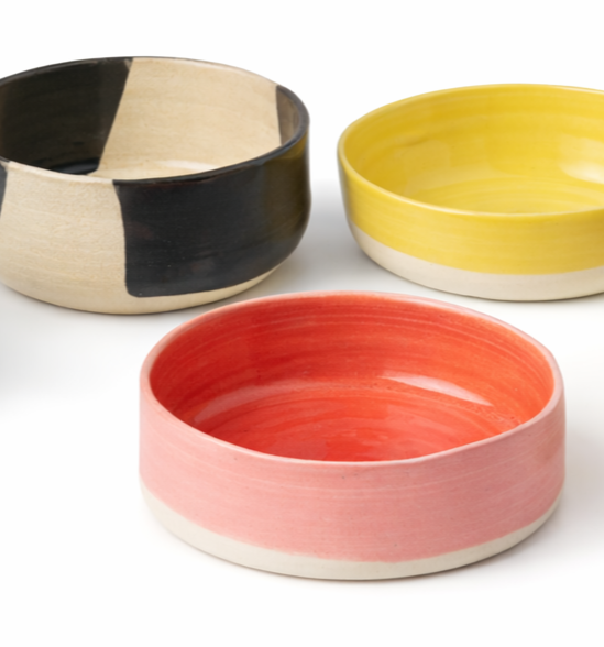 Trois bols en céramique colorés, l'un noir et beige, un jaune et un rouge
