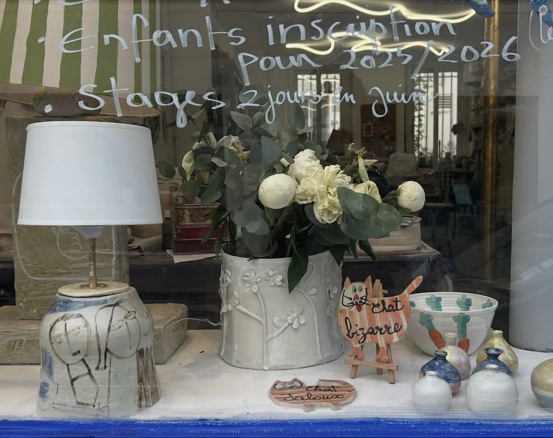 Vitrine avec une lampe, un vase avec des fleurs blanches, une figurine de chat avec inscription 'chat bizarre' et plusieurs petits vases colorés.