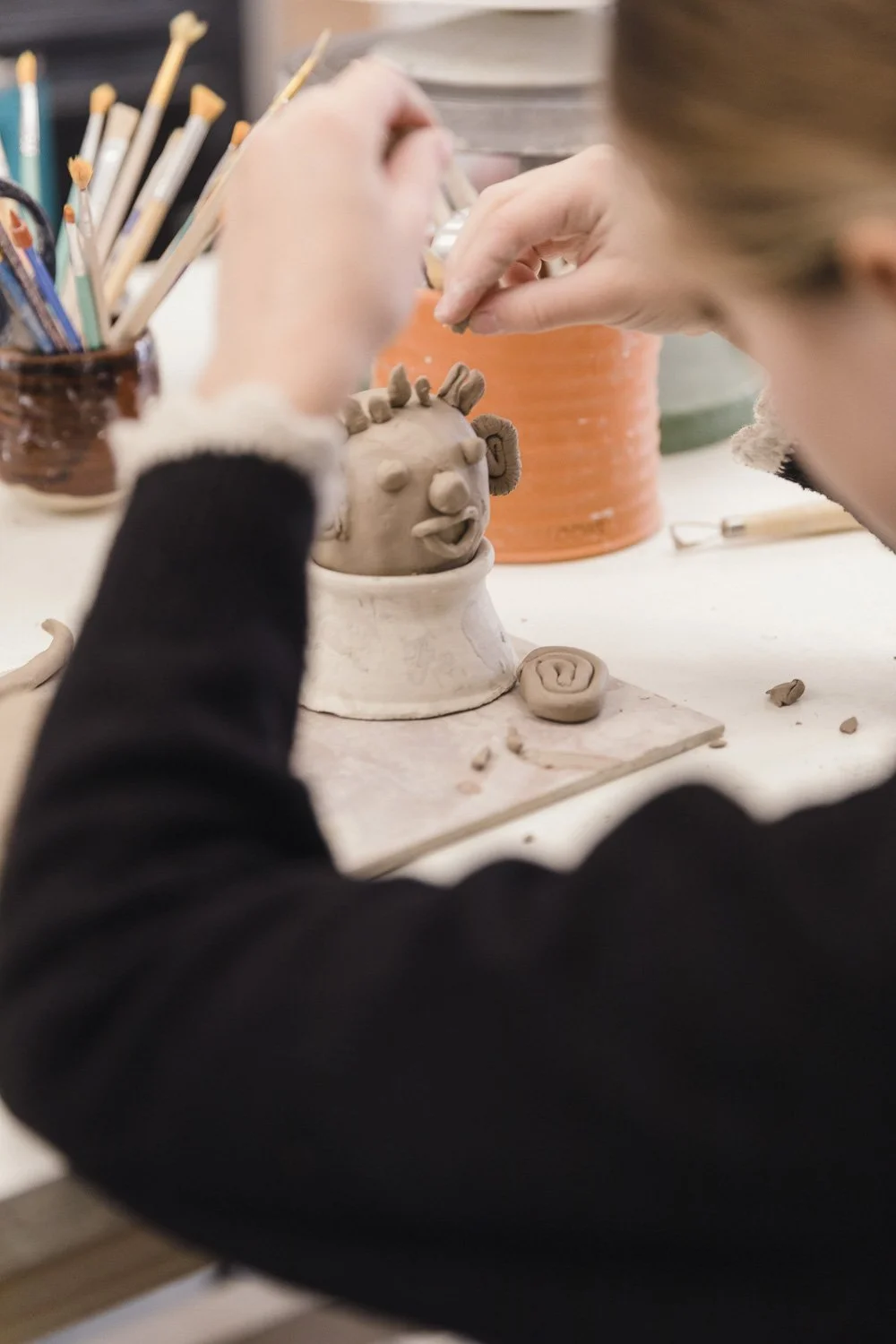 Des enfants participent à un atelier de poterie dans un studio de céramique, entourés de matériel de modelage et de pots de peinture.