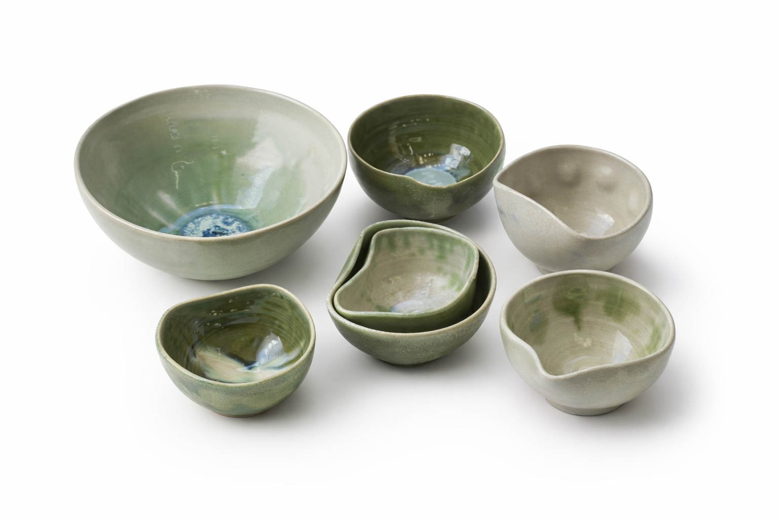 Une collection de sept bols en céramique de différentes tailles et formes, principalement en nuances de vert, avec quelques éléments décoratifs bleus à l'intérieur.
